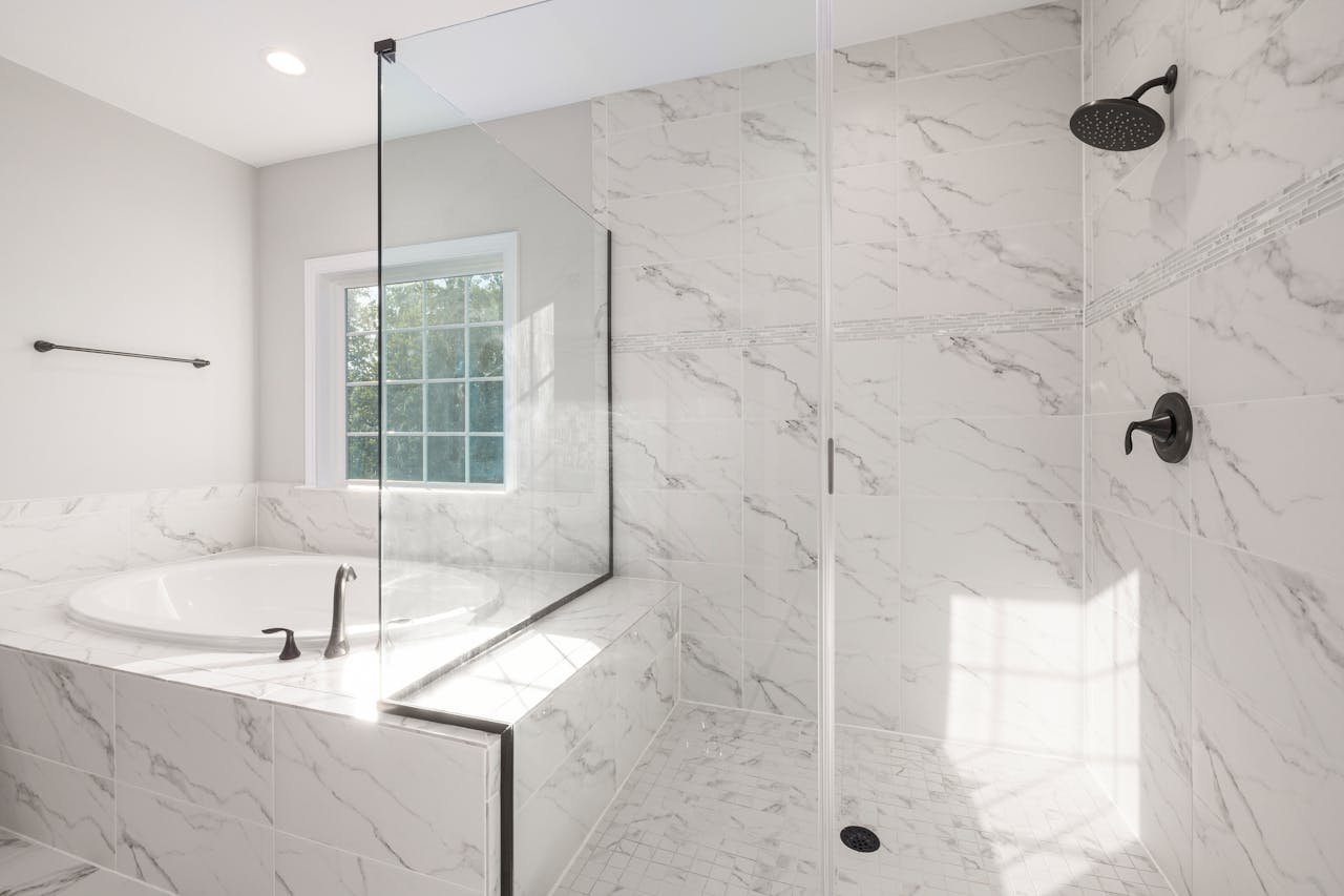 Bright marble bathroom featuring a bathtub and glass shower panel for a sleek, modern look.